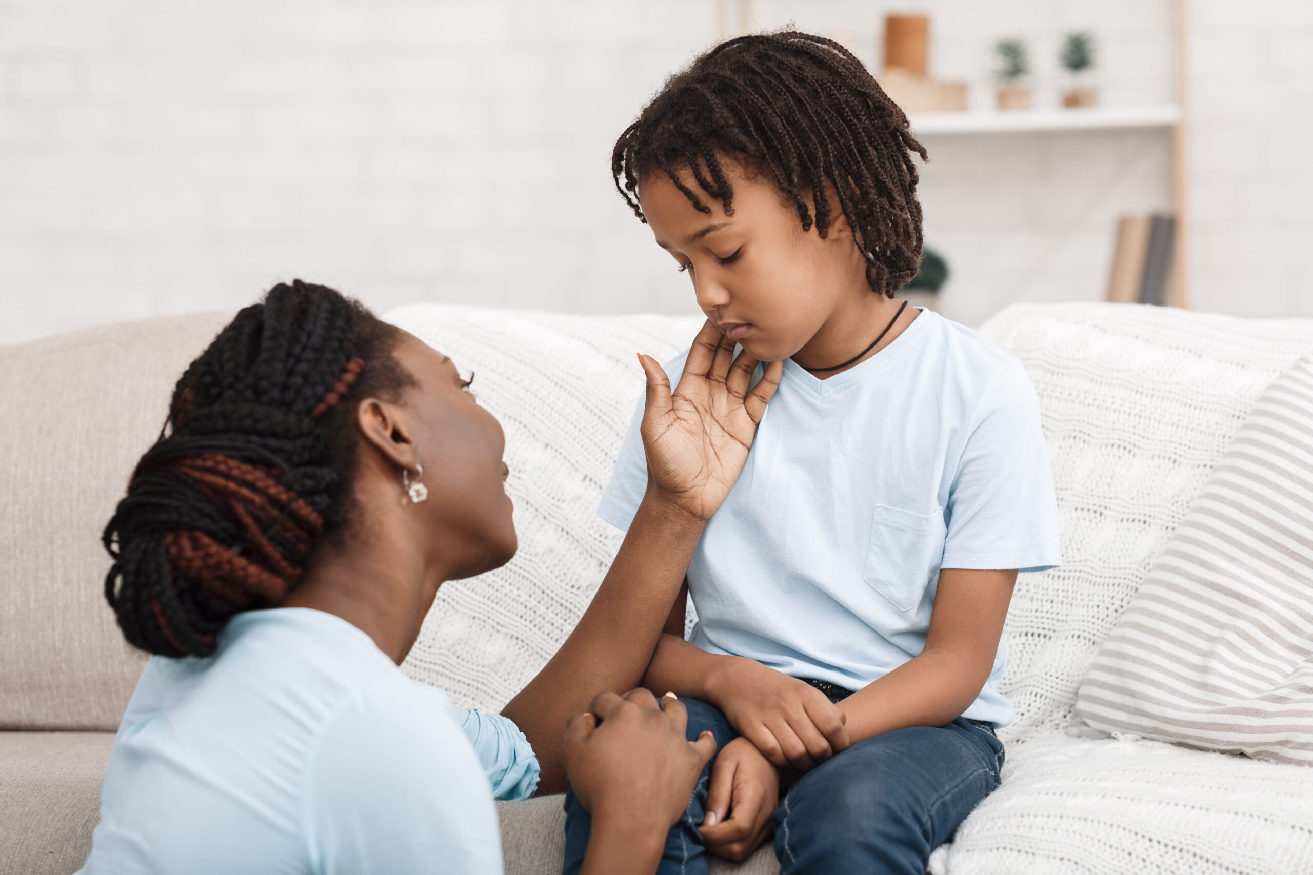 Black mom caressing her depressed kid on sofa